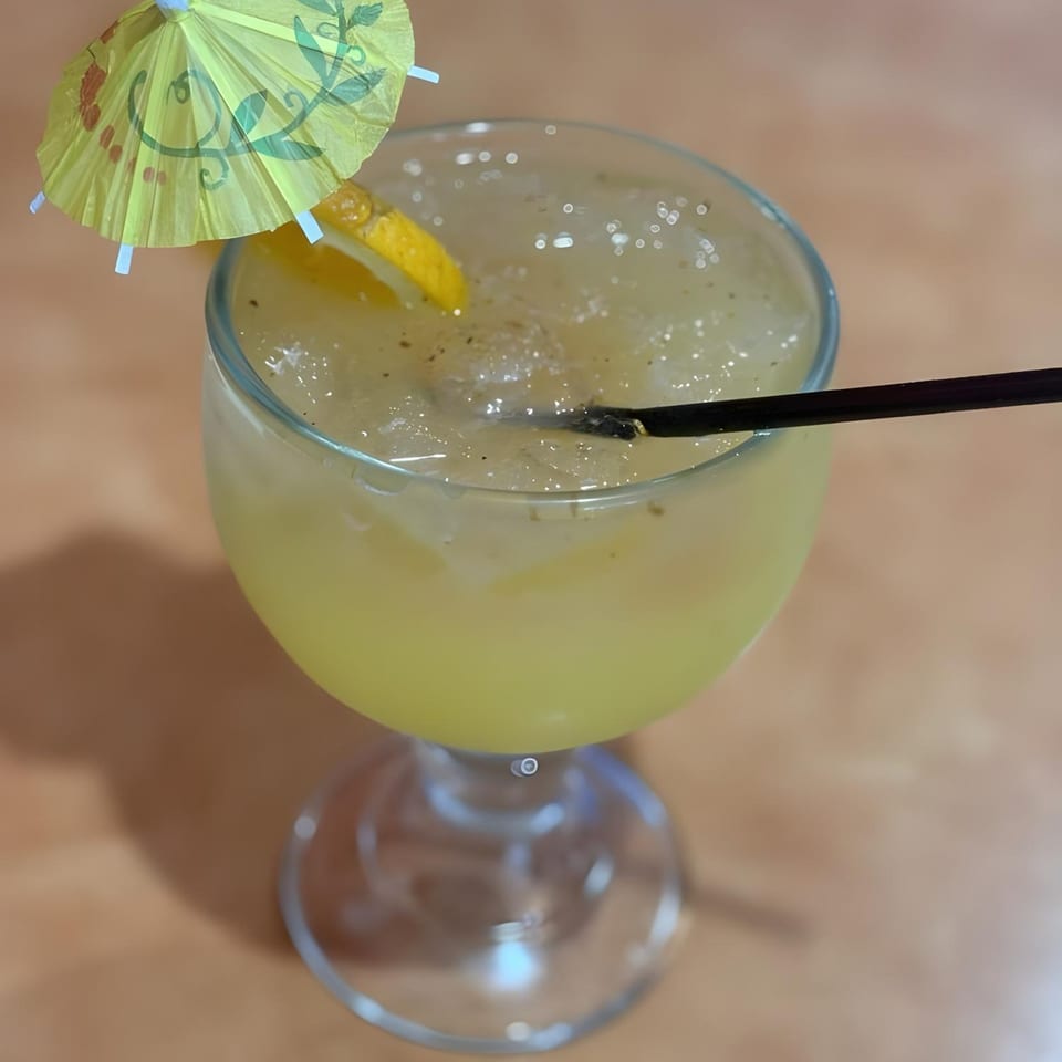 A yellow drink with ice, a lemon slice, a black straw, and a small yellow umbrella.
