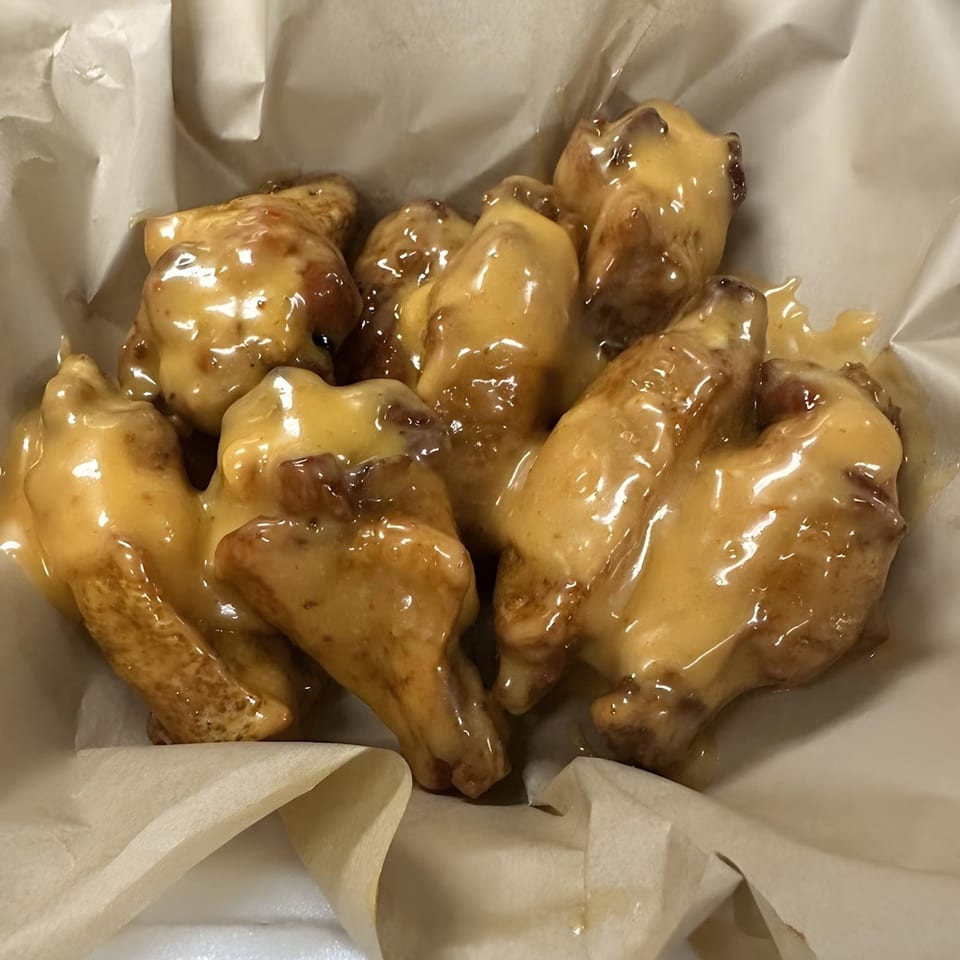 A close-up of several chicken wings coated in a thick, golden-brown sauce, served in a paper-lined container.