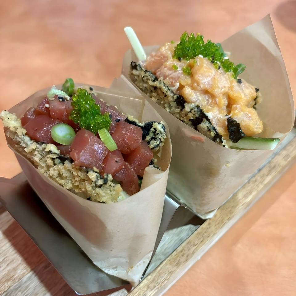 Two Asian-fusion hand rolls, one with tuna and the other with salmon, served in paper cones.